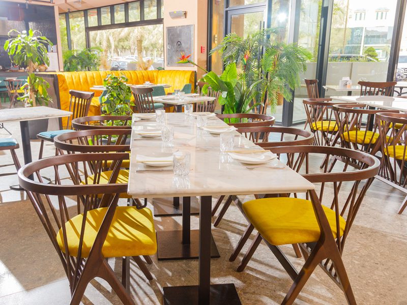 BB Social Dining Riyadh: sunny restaurant with yellow and wood chairs and marble table