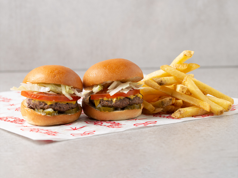 Johnny Rockets and Fat Burger delivery-only restaurants in Saudi Arabia menu: paper bag with Fatburger logo, fries, drink and cheeseburger on table: two burgers and chips on a paper napkin on a grey background