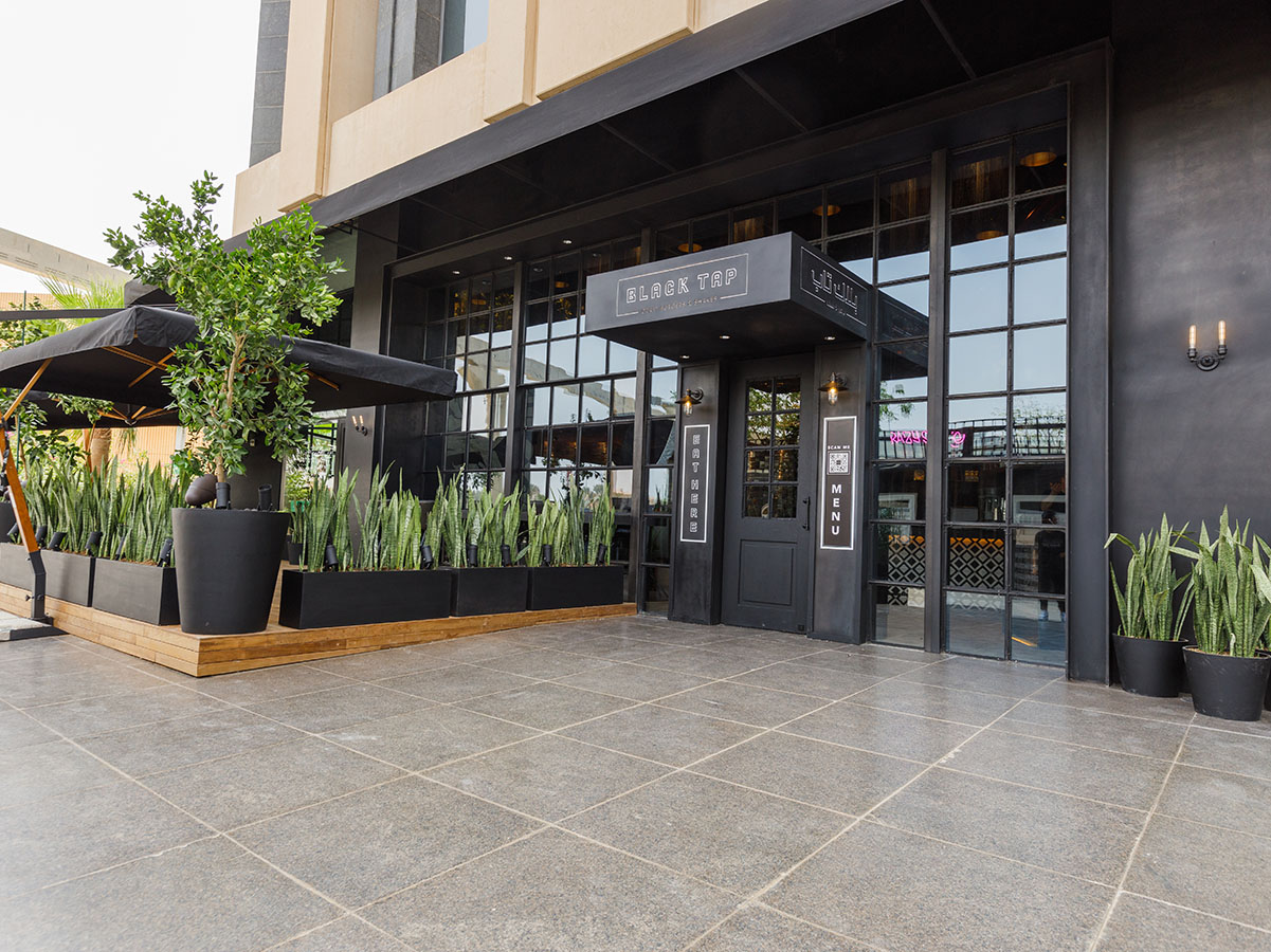 Black Tap Riyadh entrance with black storefront and patio with plants